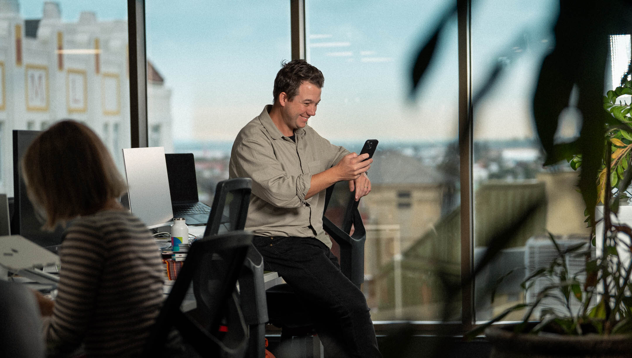 Head of client services looking at phone, with office view behind